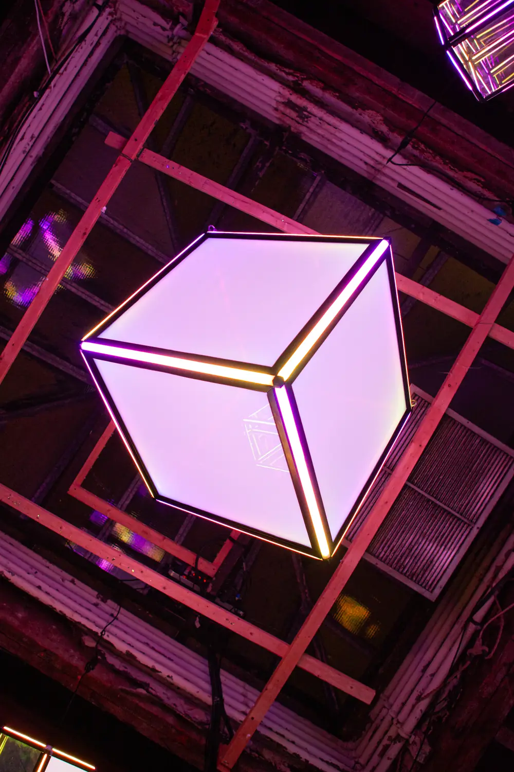 The Quantum Qube seen from below, glowing pale against the red steel rigging it hangs from.