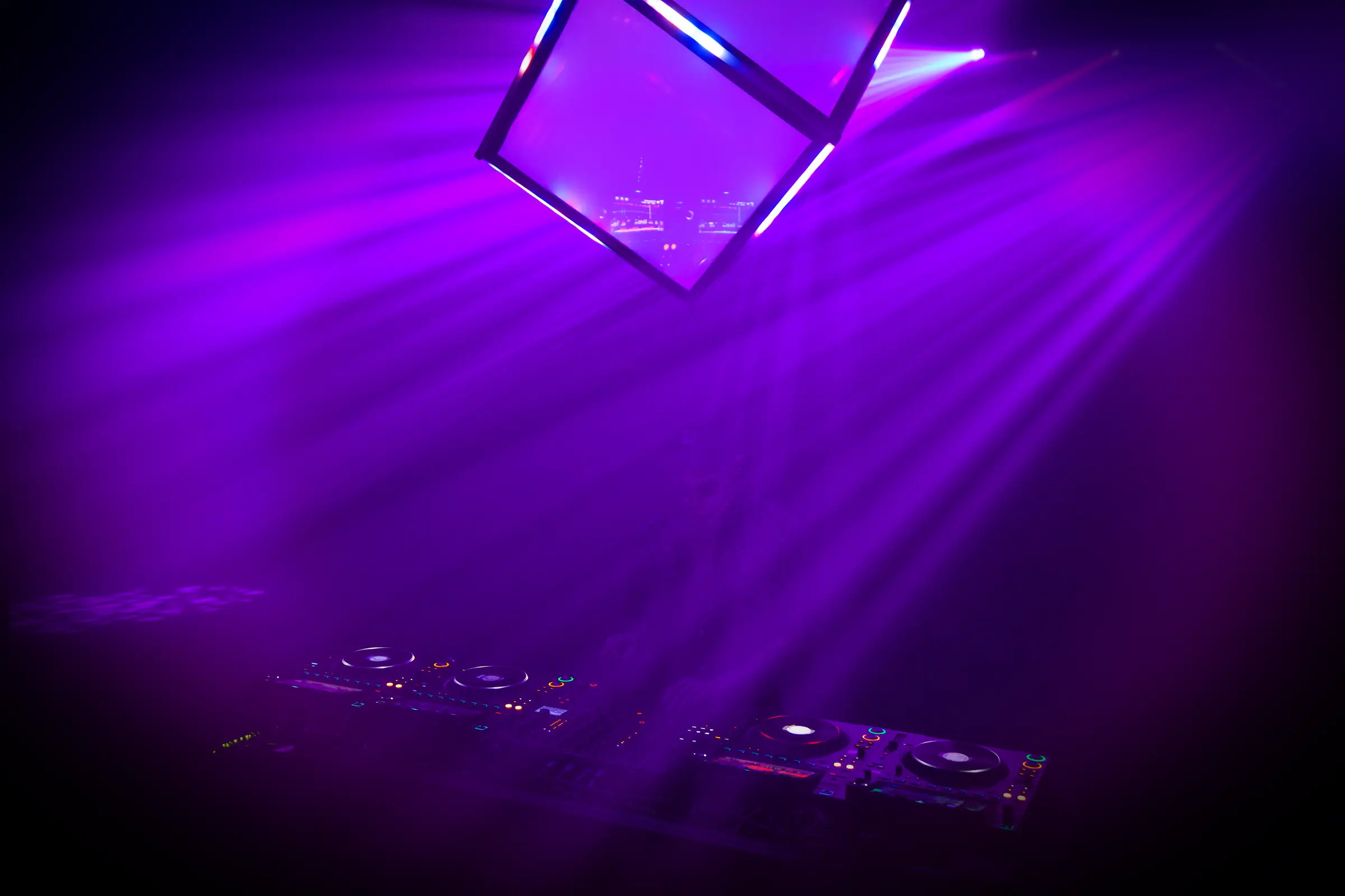 The Quantum Qube hanging above a booth in a large dark venue, violet beams fanning through heavy haze.