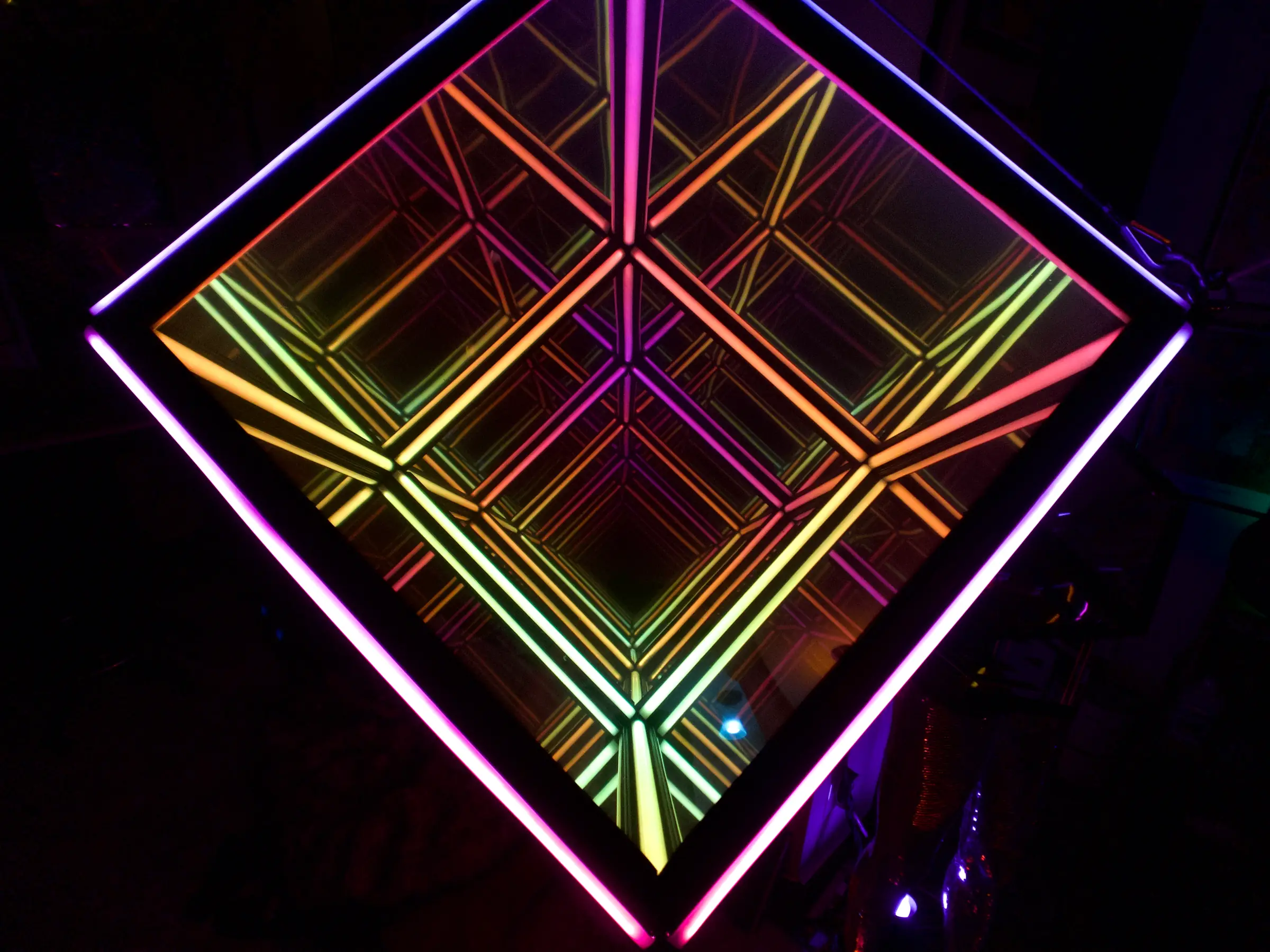 Looking up into the Qube: mirrored interior faces lit in bands of magenta, orange and green, receding into an apparently endless recursion.
