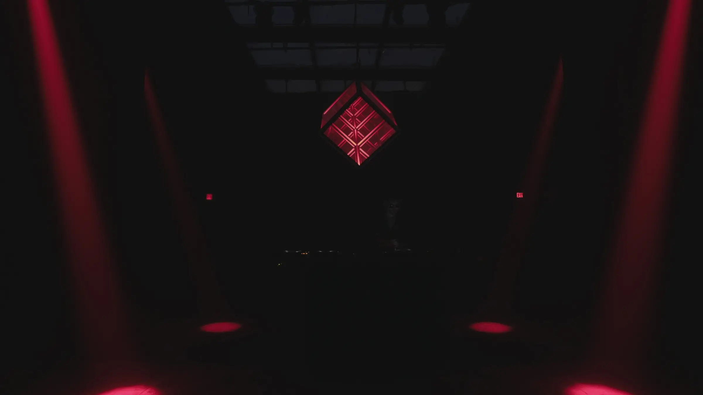 The Quantum Qube suspended above a booth in a darkened venue, lit white and flanked by symmetrical red beams cutting through haze.